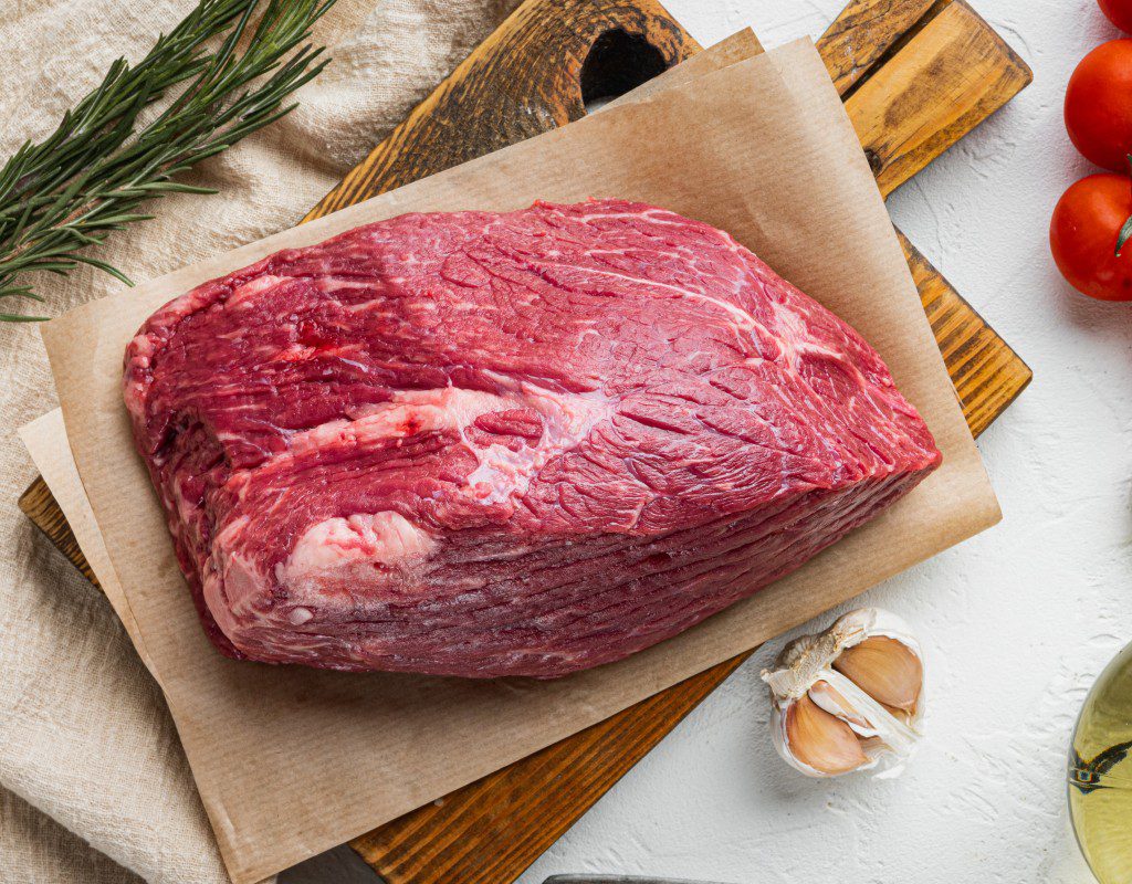 Raw beef brisket on parchment paper with garlic cloves.