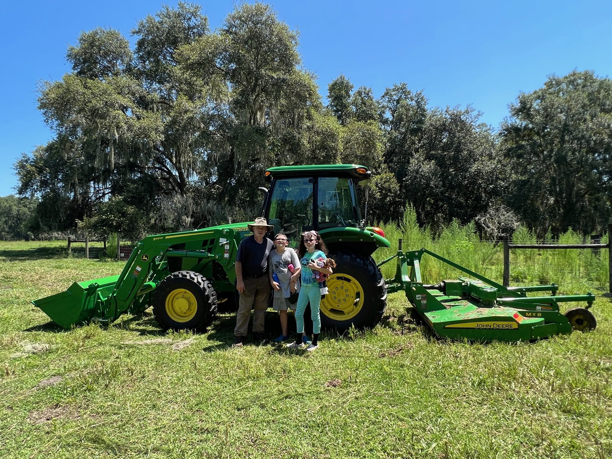 Three people standing in front of a green tractor on a sunny day.